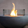 Starfire Designs Beton Round Glass Wind Guard surrounding a vibrant flame in a concrete fire pit, providing wind protection while enhancing outdoor ambiance