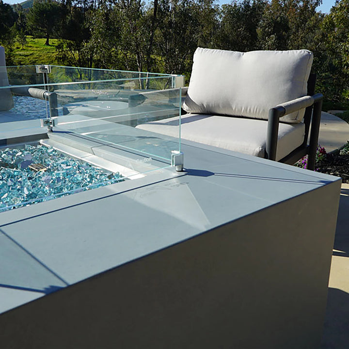 Side view of the Starfire Designs Beton Square Glass Wind Guard paired with blue fire glass. Modern design elevates outdoor fire tables, providing safety and a sleek aesthetic for patios or luxurious backyard spaces.