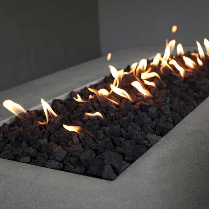 Close-up of the flame bed of the Starfire Designs Concrete Rustic 72-inch by 38-inch Rectangle Gravity Gas Fire Pit in natural gray, showcasing the natural lava rock arrangement and the consistent flame pattern that adds a cozy ambiance to any outdoor setting