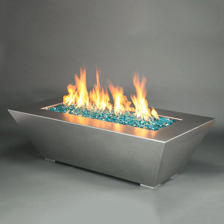 The Starfire Designs Edge Stainless Steel Gas Fire Pit in 60x32 inches, elegantly designed with clean lines and filled with striking blue fire glass. The fire pit produces vibrant flames, offering a luxurious addition to any patio or outdoor setting, combining contemporary style with high-performance functionality