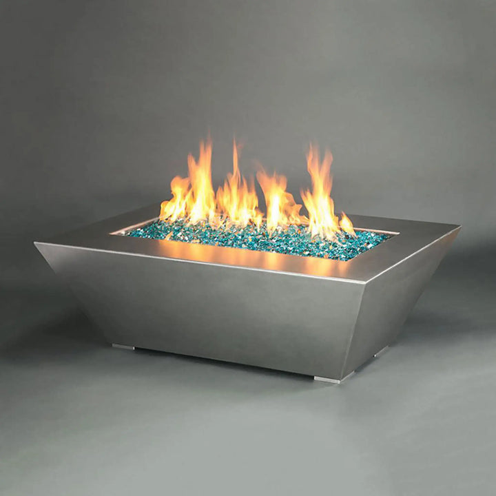 The rectangular version of the Starfire Designs Edge Stainless Steel Gas Fire Pit, showcasing an expansive bed of blue fire glass and lively flames. This fire pit is designed to provide warmth and ambiance to larger outdoor spaces, with a minimalist and sleek aesthetic that complements modern patio furniture