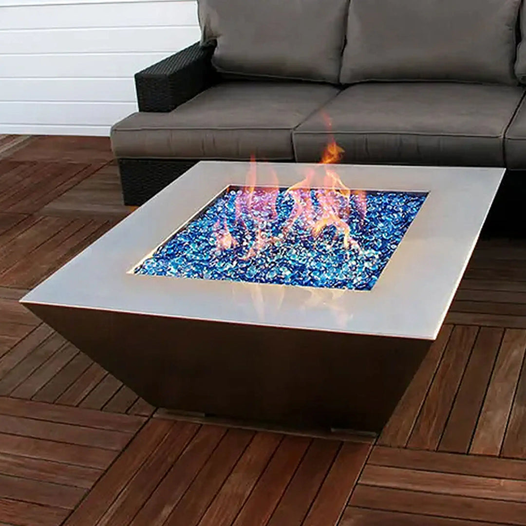 A lifestyle image of the Starfire Designs Edge Stainless Steel Square Gas Fire Pit, integrated into a cozy outdoor seating area. The fire pit, filled with blue fire glass, adds a touch of luxury and warmth to the outdoor setting, making it perfect for evening gatherings on the patio