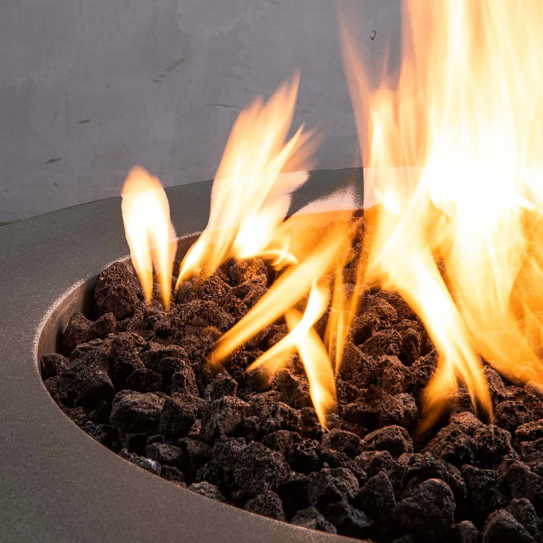 Close-up of the lava rocks and flames of the Starfire Designs Gravity 36-inch round concrete gas fire pit in brown. This close-up highlights the heat-resistant natural lava rock and the powerful flames it produces, providing an efficient and beautiful heat source for outdoor living areas. The rich brown concrete bowl adds a touch of luxury to the overall design