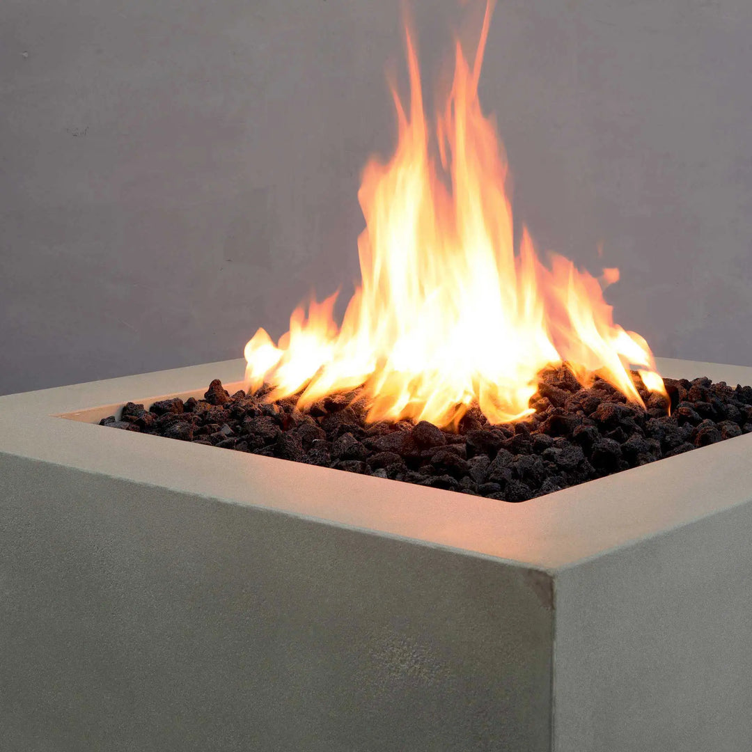 Close-up of the Starfire Designs Gravity 36" Square Concrete Gas Fire Pit's burning flame on top of black lava rocks. The beige concrete finish adds a stylish touch to outdoor settings, while the large flame provides ample warmth and ambiance for gatherings. Durable and weather-resistant, it's perfect for any outdoor space.