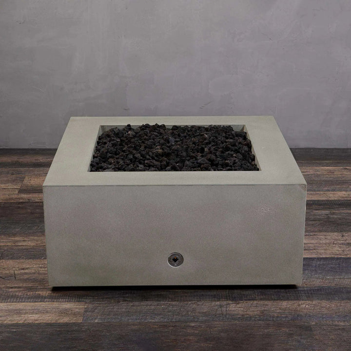  A view of the Starfire Designs Gravity 36" Square Concrete Gas Fire Pit in beige, without flames. The dark lava rocks rest in the square basin, ready for ignition. Its minimalist, robust design makes it a great addition to any patio or outdoor area, blending aesthetics with functionality.