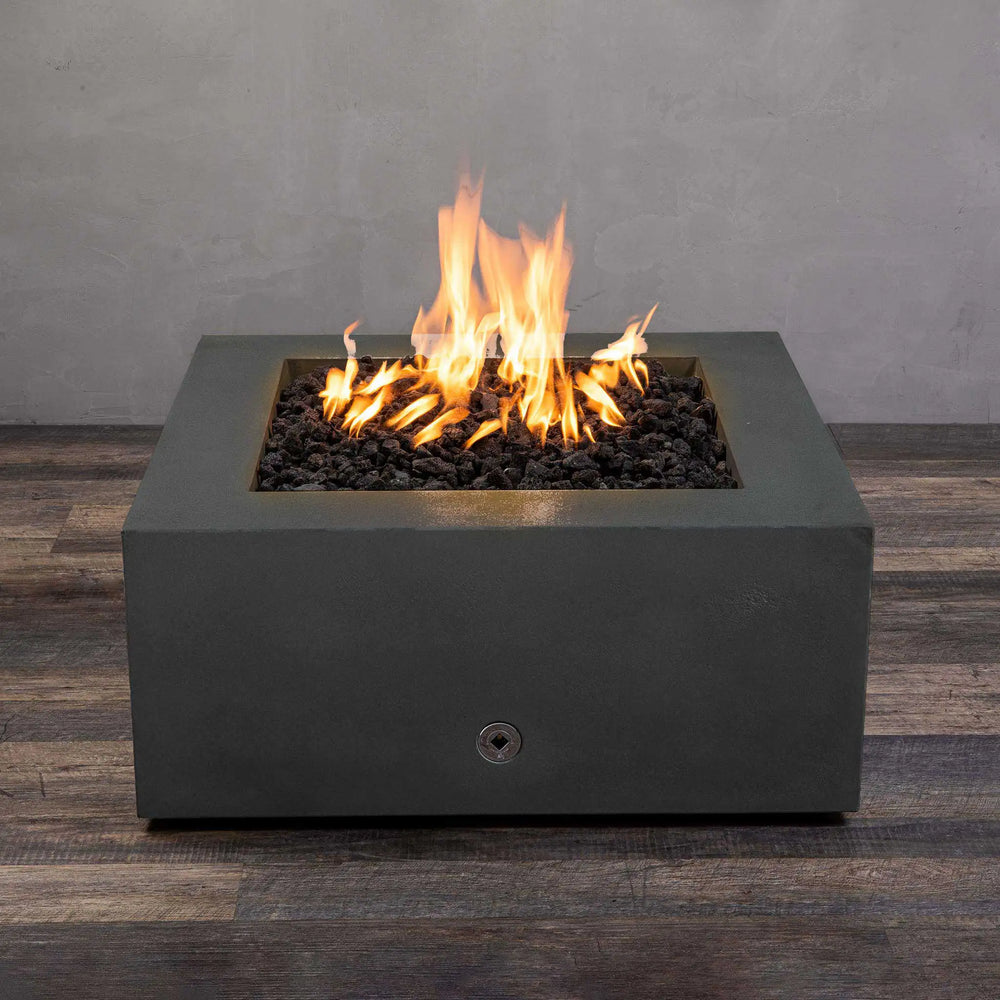 Side view of the Starfire Designs Gravity 36-inch Square Concrete Gas Fire Pit in Graphite with vibrant flames rising from a bed of black lava rocks. The robust square fire pit is designed with a contemporary aesthetic, providing warmth and ambiance for outdoor living spaces. Ideal for high-end outdoor décor and garden setups