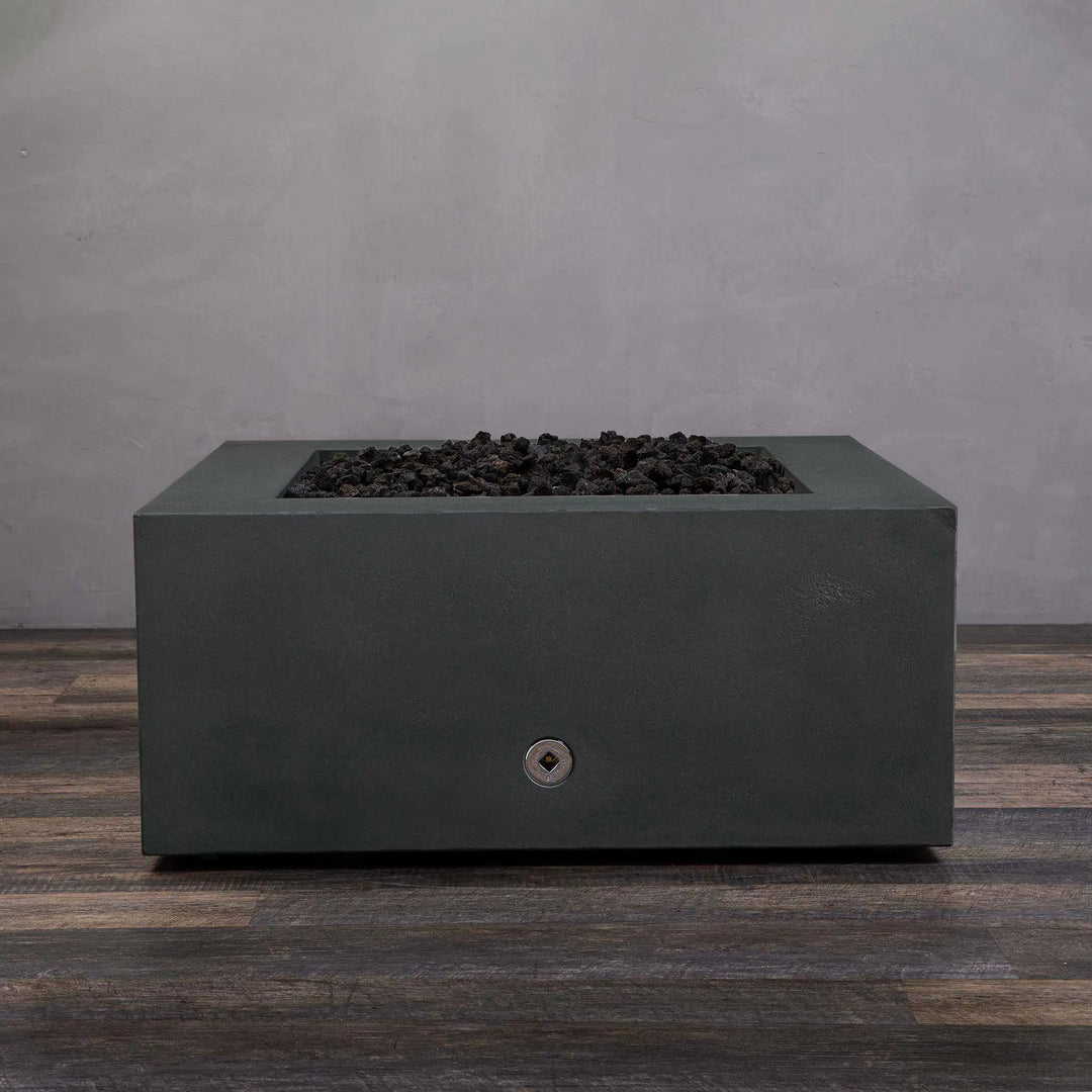 Graphite Starfire Designs Gravity 36-inch Square Concrete Gas Fire Pit with lava rocks but no flames. This modern gas fire pit blends seamlessly into outdoor environments, offering a sleek and stylish option for patios or gardens. Its dark graphite finish gives it a bold presence even when not in use.