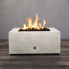 A front view of the Starfire Designs Gravity 36" Square Concrete Gas Fire Pit in white, featuring a robust flame rising from the fire pit’s lava rock fill. The sleek, modern concrete design complements outdoor spaces and is perfect for both residential and commercial use