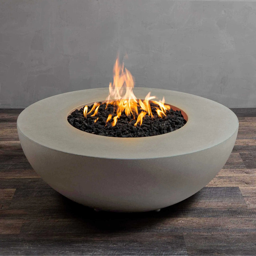 The Starfire Designs Gravity 45" round concrete gas fire pit in beige, featuring a medium flame rising from a bed of black lava rocks. The sturdy beige concrete construction complements modern and rustic outdoor settings, providing warmth and ambiance. This fire pit is built for residential or commercial use, ensuring long-lasting performance