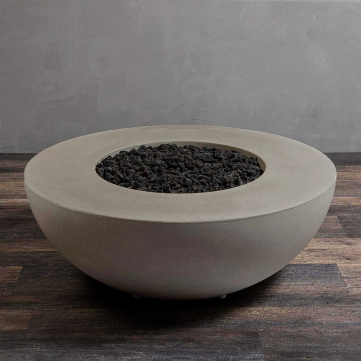 An unlit Starfire Designs Gravity 45" round concrete gas fire pit in beige, showcasing the dark lava rocks inside the smooth beige concrete bowl. This fire pit combines modern design with high durability, making it a perfect addition to any backyard or commercial patio.