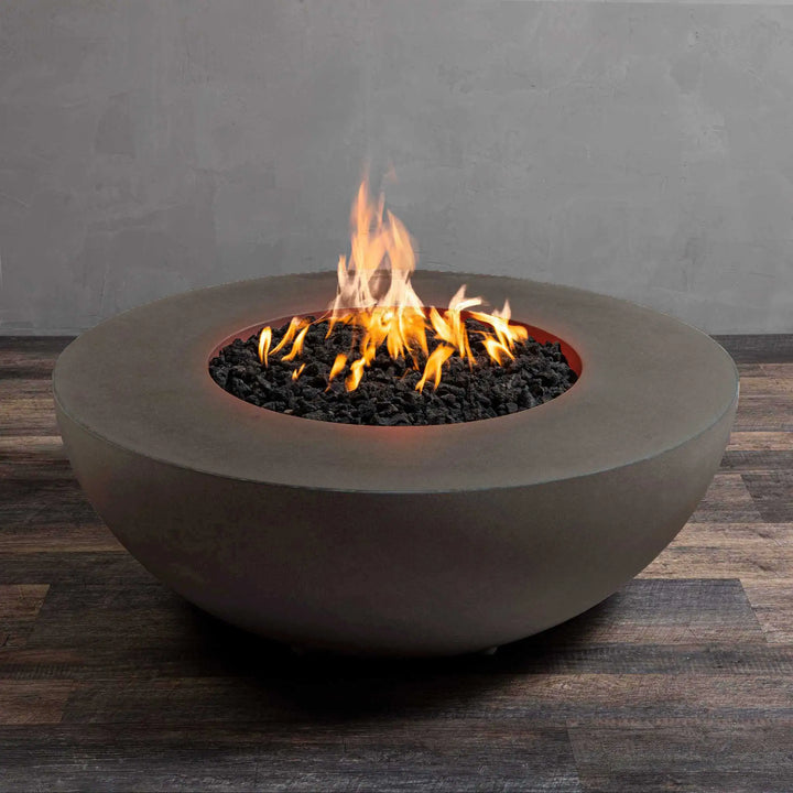 Angled view of the Starfire Designs Gravity 45-inch round gas fire pit in brown with flames. This concrete fire pit showcases its contemporary bowl shape and sleek design, ideal for outdoor entertaining. Features natural brown finish and premium gas burner with lava rock