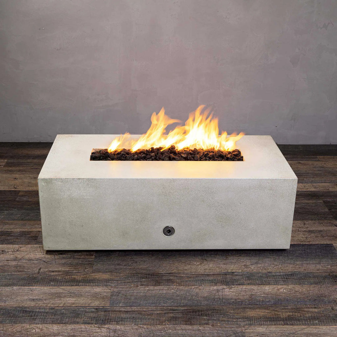 Angled view of the white Starfire Designs Gravity 48" x 32" Rectangle Concrete Gas Fire Pit with flames blazing from its long linear burner. The fire pit's contemporary rectangular design is highlighted, with a clean concrete finish perfect for upscale outdoor living spaces