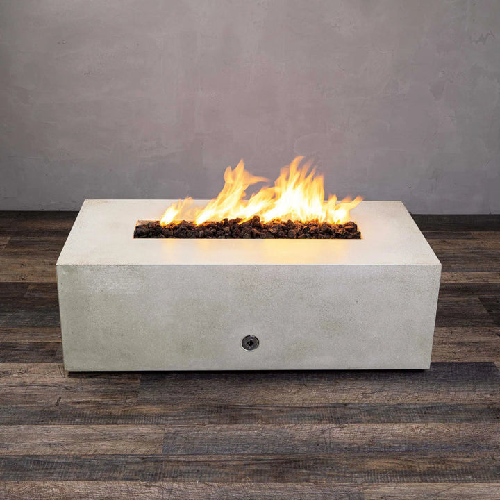 Angled view of the white Starfire Designs Gravity 48" x 32" Rectangle Concrete Gas Fire Pit with flames blazing from its long linear burner. The fire pit's contemporary rectangular design is highlighted, with a clean concrete finish perfect for upscale outdoor living spaces