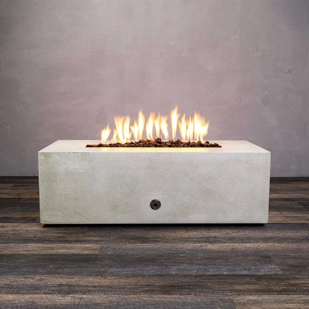 A white concrete Starfire Designs Gravity 48" x 32" Rectangle Gas Fire Pit with bright flames rising from the linear burner. The modern design contrasts with the gray backdrop, showcasing the fire pit's sleek look. Ideal for outdoor settings, this fire pit is built with durable materials, making it suitable for any weather.