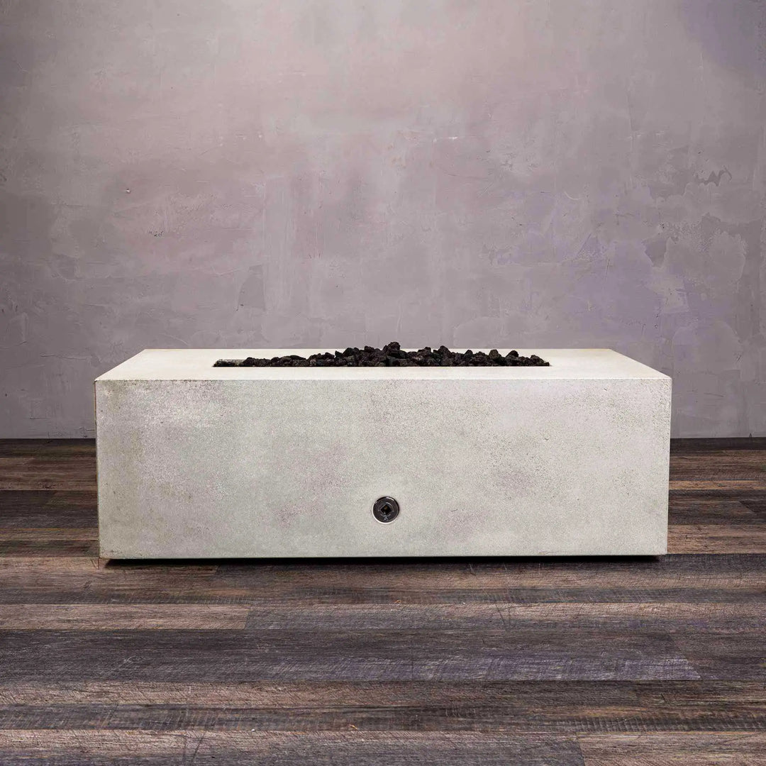 The Starfire Designs Gravity 48" x 32" Rectangle Gas Fire Pit in white, with lava rocks surrounding the linear burner. The sleek concrete finish and functional burner are designed to blend with high-end outdoor decor.