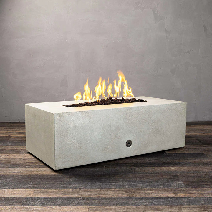 A side view of the Starfire Designs Gravity 48" x 32" Rectangle Gas Fire Pit in white concrete, showcasing a long flame bed filled with lava rocks. The sleek design complements modern patio aesthetics, delivering both style and warmth.