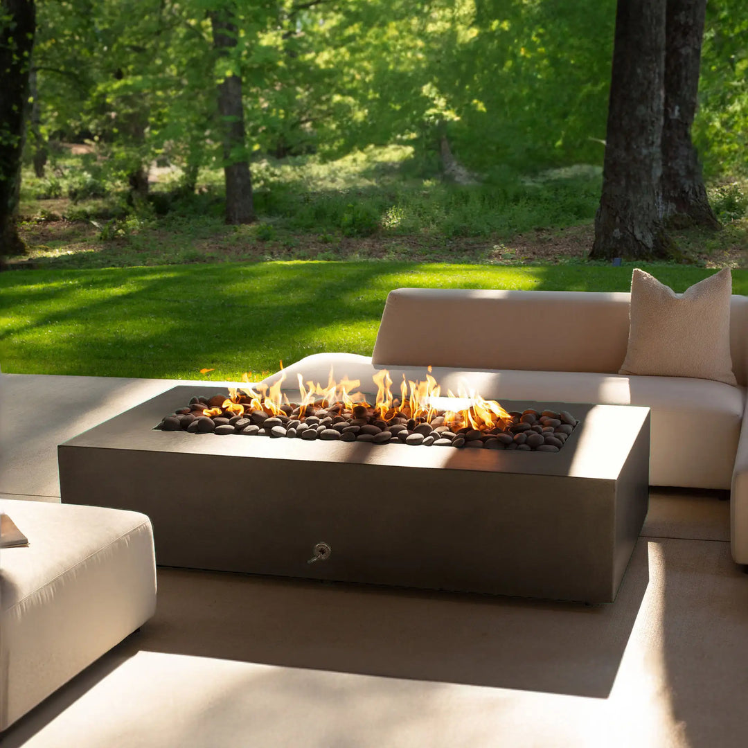 Cozy outdoor scene with the Starfire Designs Gravity 60" x 32" Rectangle Concrete Gas Fire Pit in brown, placed alongside plush seating. The inviting flames enhance the ambiance.