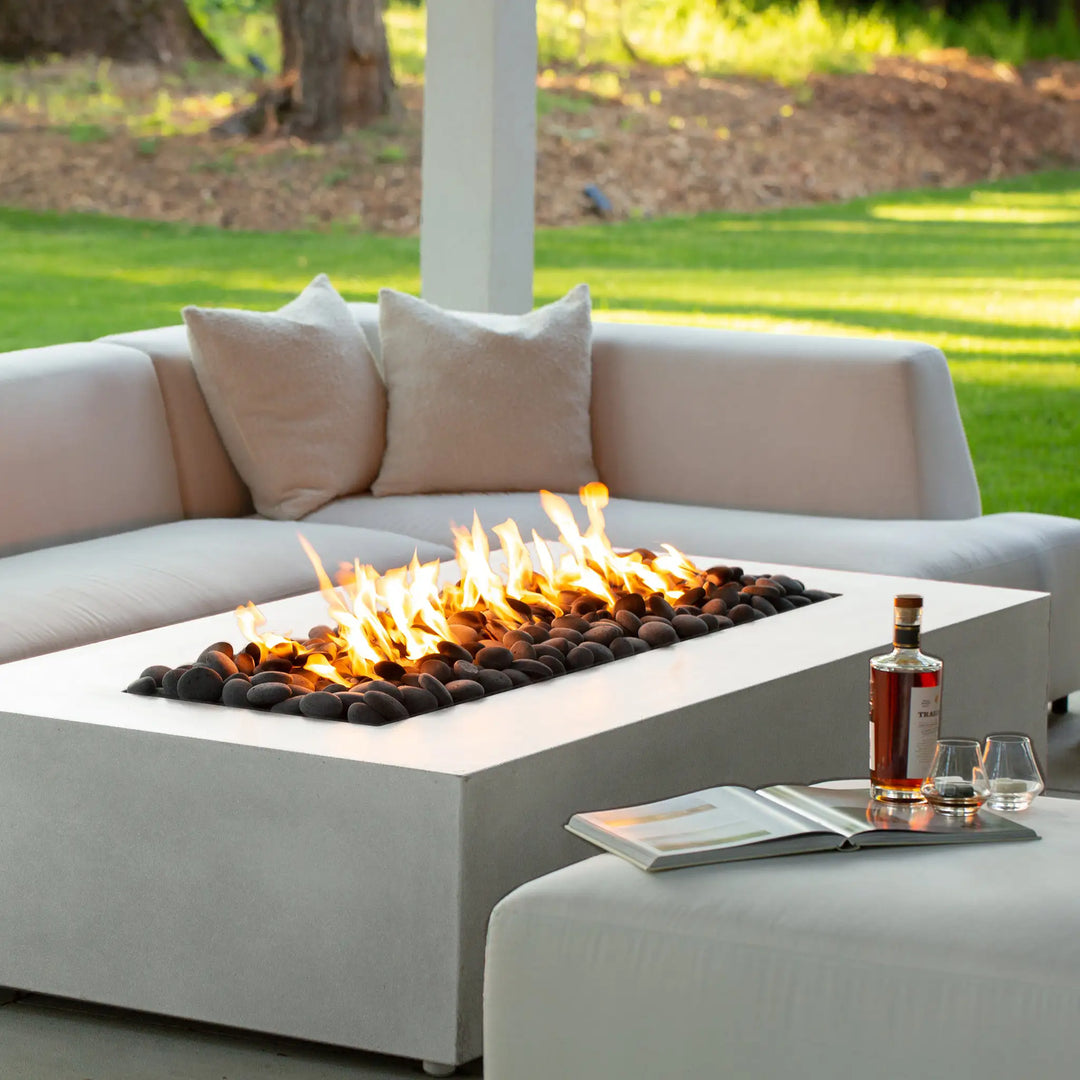 A close-up lifestyle image of the Starfire Designs Gravity 60" x 32" Rectangle Concrete Gas Fire Pit in white, with a cozy flame burning. The fire pit’s sleek concrete surface and minimalist design make it a centerpiece for any backyard or patio area.