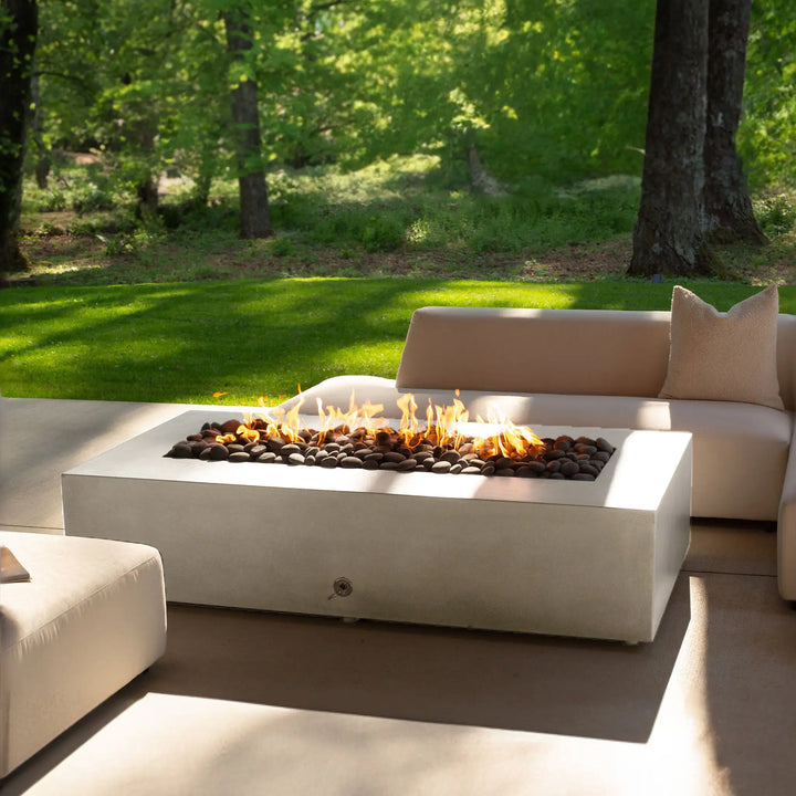 A lifestyle scene showcasing the Starfire Designs Gravity 60" x 32" Rectangle Concrete Gas Fire Pit in white, placed on a modern patio surrounded by outdoor seating. The fire pit provides warmth and style, perfect for gatherings in a beautifully designed outdoor space.