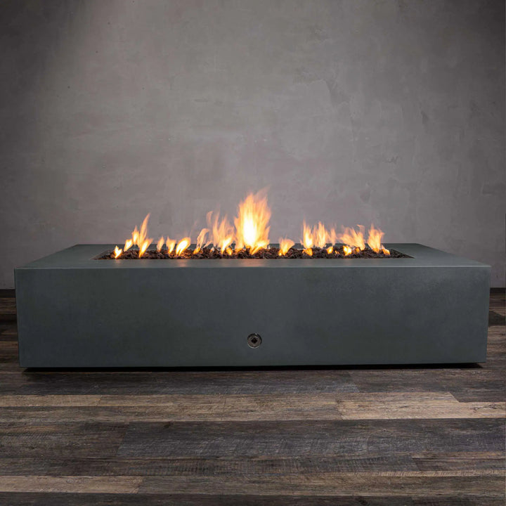 Starfire Designs Gravity 72-inch by 38-inch rectangular concrete gas fire pit in a deep graphite finish, shown from a side angle with vibrant flames rising above the lava rock-filled burner. This modern and sleek outdoor fire feature is made of durable, weather-resistant concrete and adds a touch of luxury and warmth to any patio setting. Perfect for outdoor entertaining, this fire pit combines elegant design with powerful heat output.