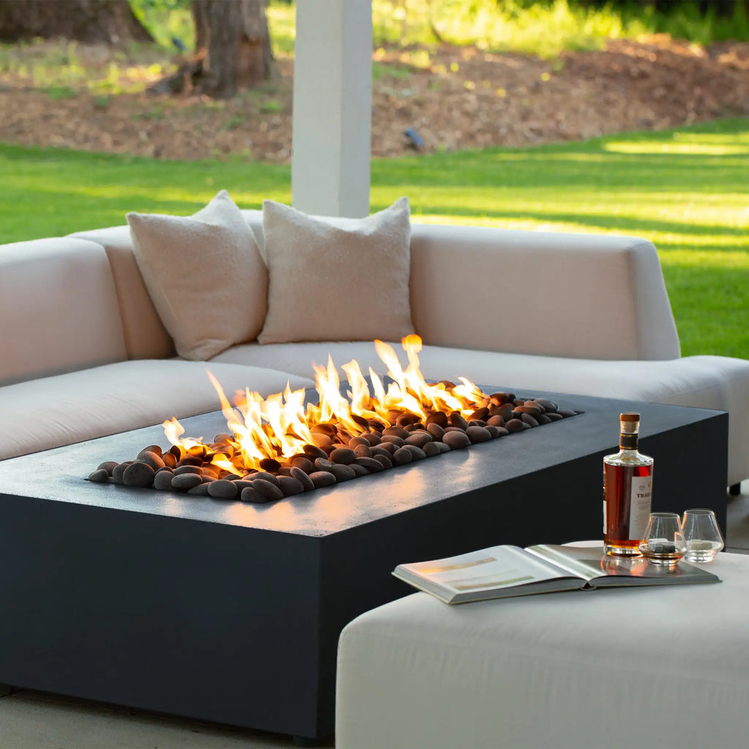 A cozy outdoor setting featuring the Starfire Designs Gravity 72-inch by 38-inch graphite concrete gas fire pit, with flickering flames and contemporary furniture, creating a warm and inviting atmosphere. The rectangular fire pit's modern design and powerful flame make it a stylish and functional addition to any outdoor living space. Perfect for creating a focal point in high-end patio environments.