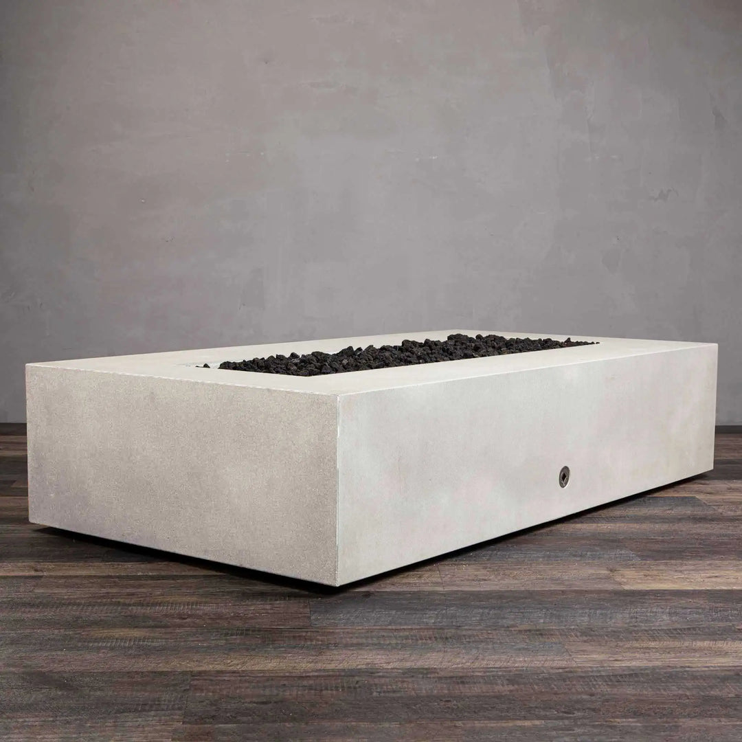 Angled side view of the Starfire Designs Gravity 72 x 38 inch rectangle concrete gas fire pit in white, displaying a smooth and minimalist concrete structure with flames in the center surrounded by black lava rocks. This fire pit is designed to elevate any outdoor patio or commercial space with its clean, modern lines and durable construction. White concrete fire pit, angled view, modern outdoor heating solution