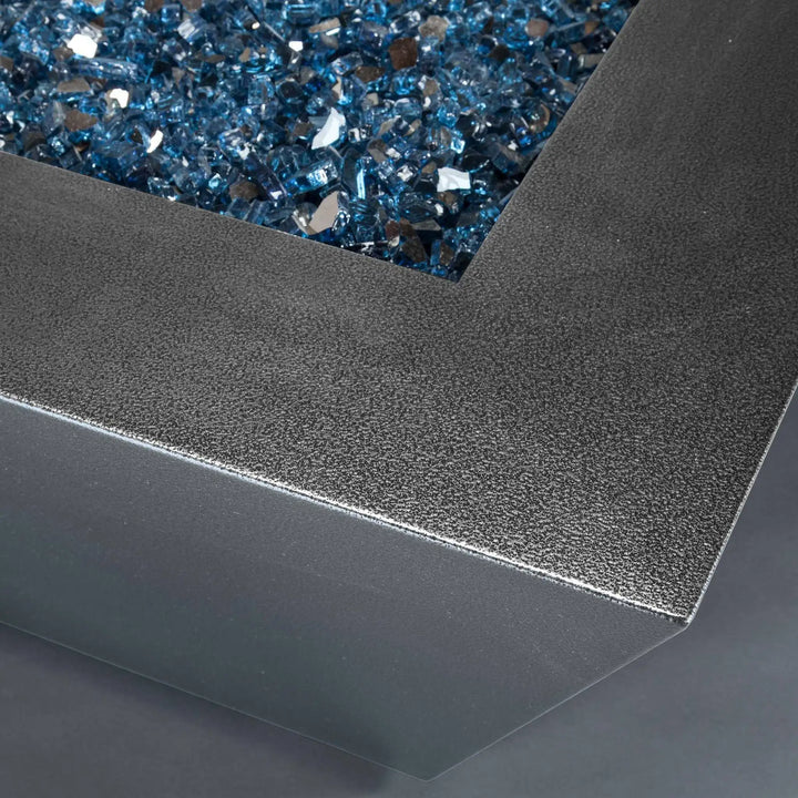 Close-up of Starfire Designs Mill 48-inch square gas fire pit in Silver Hammertone, highlighting the textured steel finish and vibrant blue fire glass, a stylish centerpiece for modern outdoor spaces