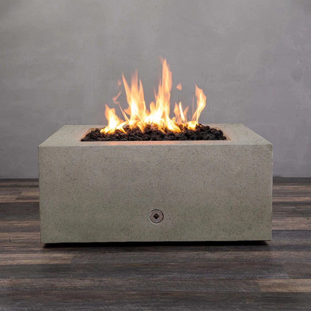 Full view of the Starfire Designs Rustic Gravity 36-inch Square Concrete Gas Fire Pit in beige with a vibrant flame, placed on a wooden deck with a grey wall backdrop