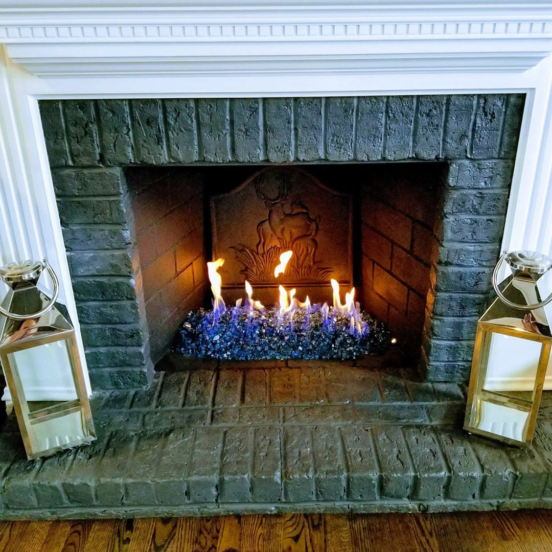 A cozy indoor fireplace featuring Starfire Glass 1/2" Broken Fire Glass (10lbs) in Pacific Blue Reflective. The reflective fire glass enhances the dancing flames, providing a contemporary and elegant alternative to traditional logs. Ideal for ventless fireplaces, gas log replacements, and modern fire features, this fire glass offers a clean, smoke-free, and maintenance-free solution.