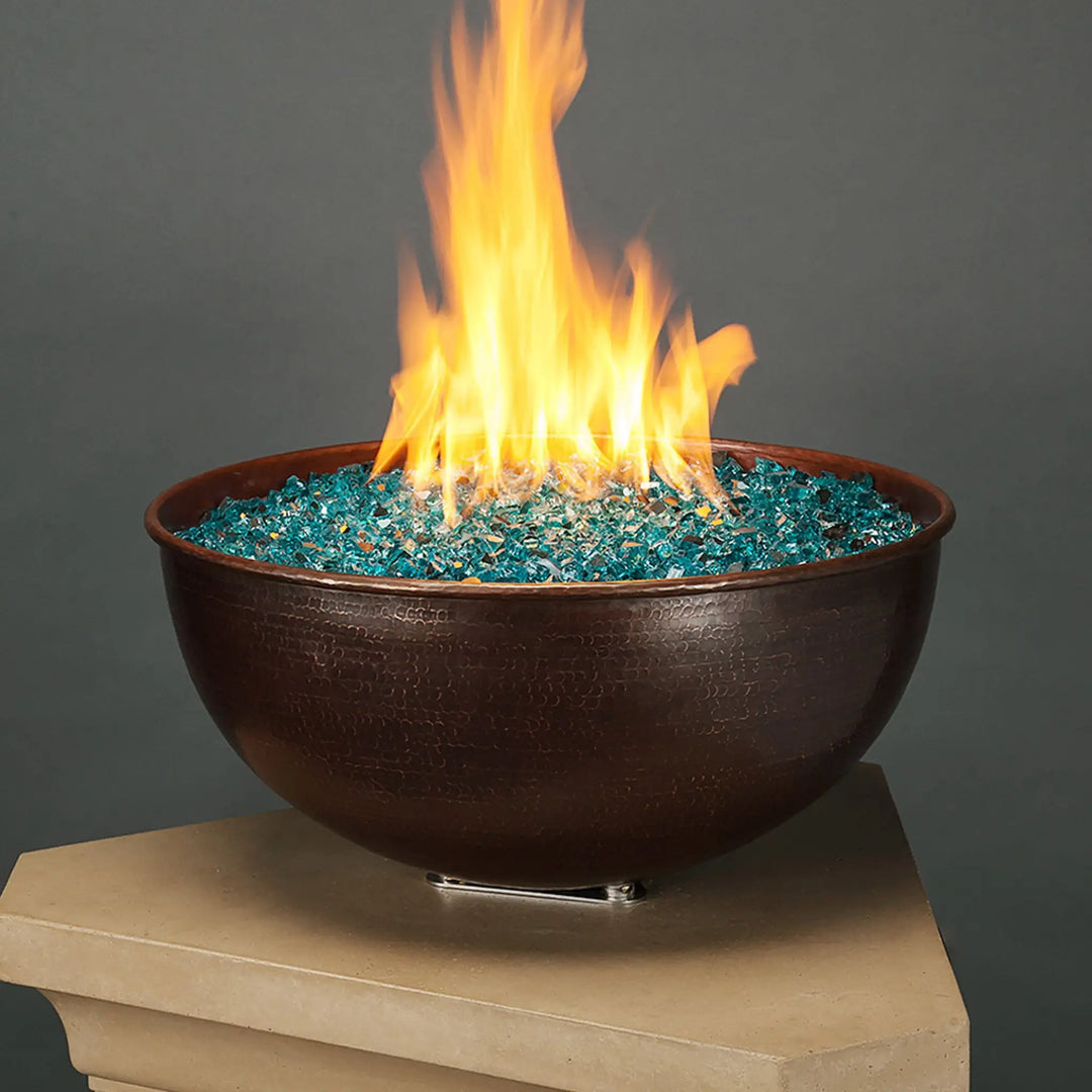 A stunning hammered copper fire bowl filled with Starfire Glass 1/2" Broken Fire Glass (10lbs) in Pacific Blue Reflective. The vibrant blue reflective fire glass enhances the flame’s brilliance, making it an eye-catching feature for any outdoor fire pit. The reflective surface maximizes light reflection, creating a luxurious ambiance. Ideal for fire bowls, propane fire pits, and modern outdoor spaces.