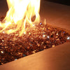 A close-up view of a rectangular fire pit showcasing amber-colored Starfire Glass 1/4" broken fire glass (10lbs) glowing intensely under dancing flames. Adds warmth and elegance to outdoor spaces.