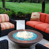 A cozy backyard seating area with a copper fire bowl filled with shimmering Starfire Glass 1/4" broken fire glass (10lbs), glowing softly among woven chairs and colorful cushions. Ideal for outdoor relaxation. 