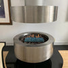 A contemporary stainless steel fire pit filled with blue Starfire Glass 1/4" broken fire glass (10lbs), designed with a sleek circular frame and glowing brightly. Perfect for modern interiors.