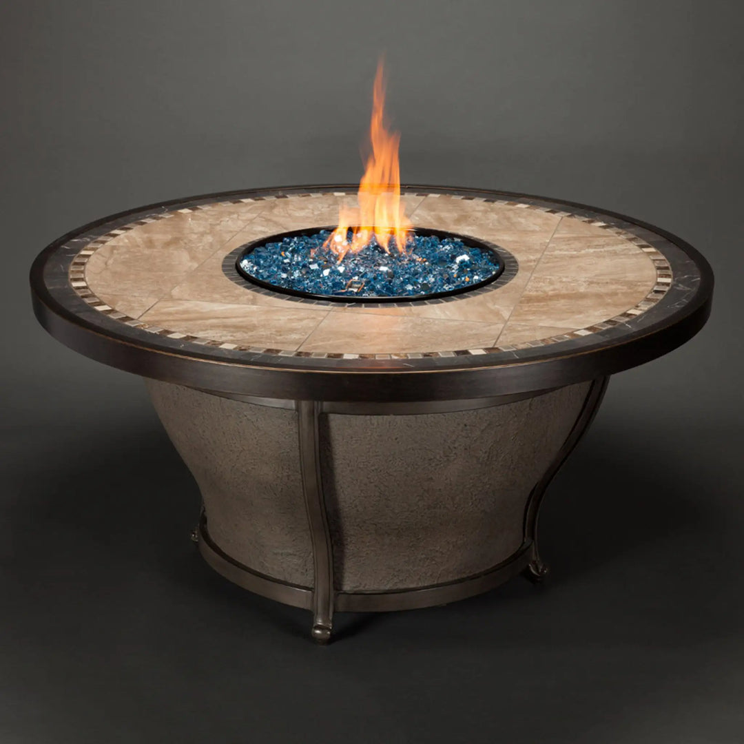 A classic round fire table with a tiled top and elegant design, featuring blue Starfire Glass 1/4" broken fire glass (10lbs) glowing under a flame. Ideal for enhancing a patio or backyard space with style and functionality. 