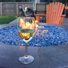 A vibrant backyard patio featuring a round fire pit filled with sparkling blue Starfire Glass 1/4" broken fire glass (10lbs). A glass of white wine rests on the fire pit edge, creating a cozy and inviting outdoor ambiance.