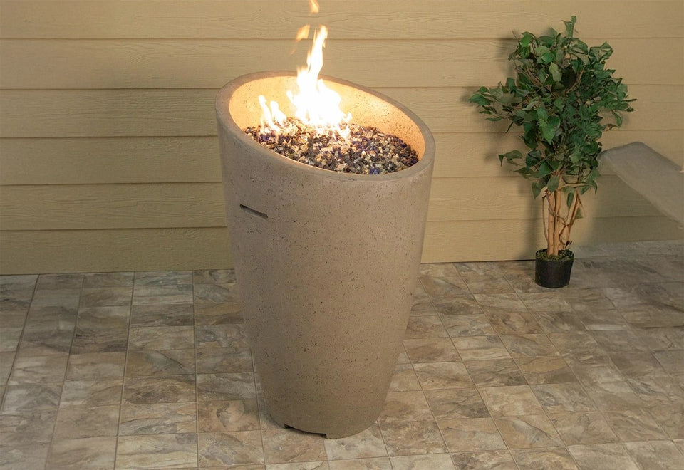 Modern tall tan concrete fire pit column with a sleek tapered design and vibrant flames. The fire column features mixed glass fire media, adding a touch of elegance to outdoor patios and contemporary backyard settings, providing warmth and ambiance for alfresco entertaining.