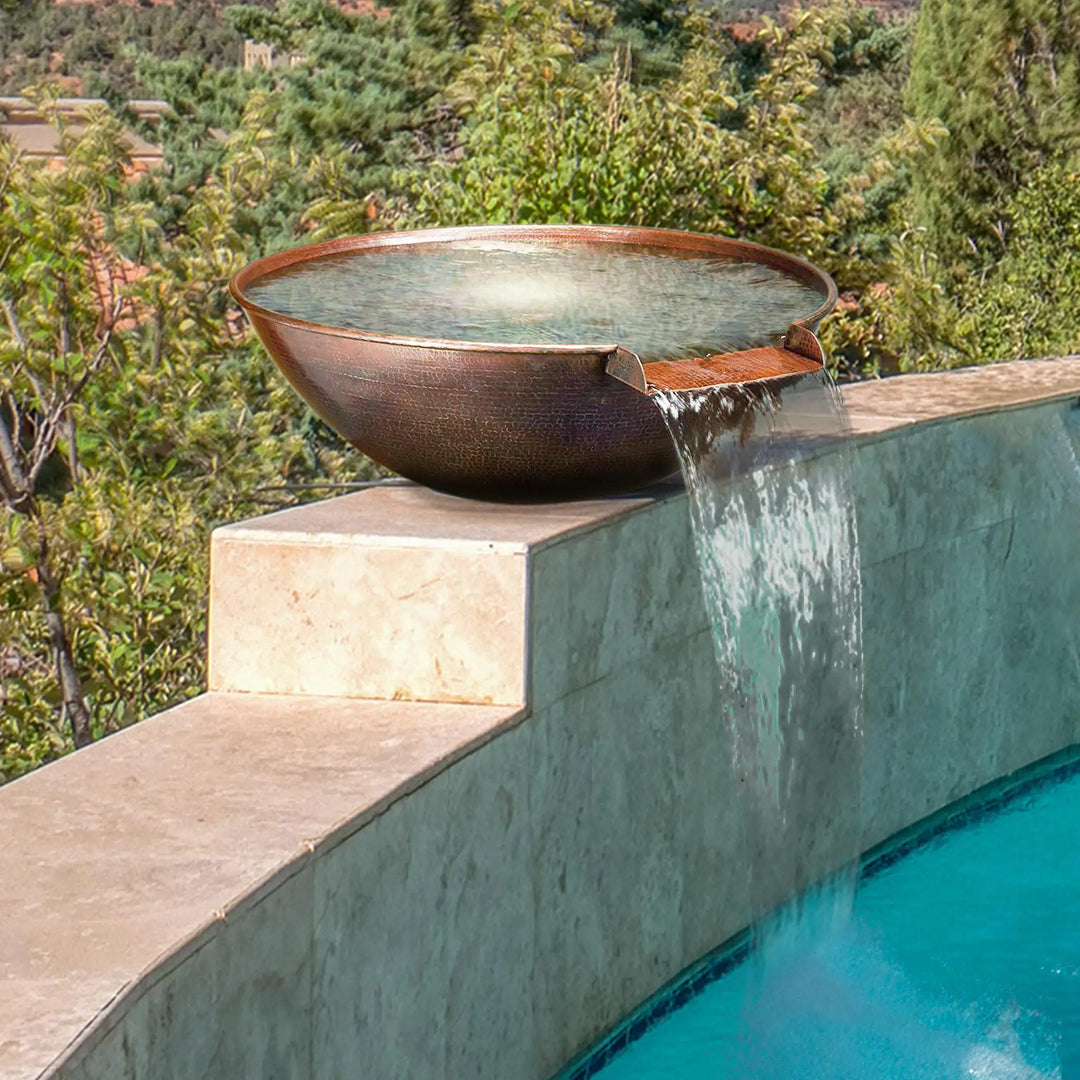 Taza Moreno 30-inch round copper water bowl installed on a poolside stone pedestal, featuring a cascading water flow, ideal for enhancing luxury outdoor landscapes by Starfire Designs