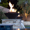 The Outdoor Plus 31-inch Round Concrete Cazo Fire Bowl at night, beautifully lit and placed on a raised stone platform with cascading water. The sleek black concrete finish enhances the bowl’s modern design, making it a perfect addition to luxury backyard landscaping. Fire from the bowl creates a warm, inviting ambiance. Round concrete fire bowl, outdoor fire feature, nighttime fire bowl, luxury fire pit, outdoor fire and water feature