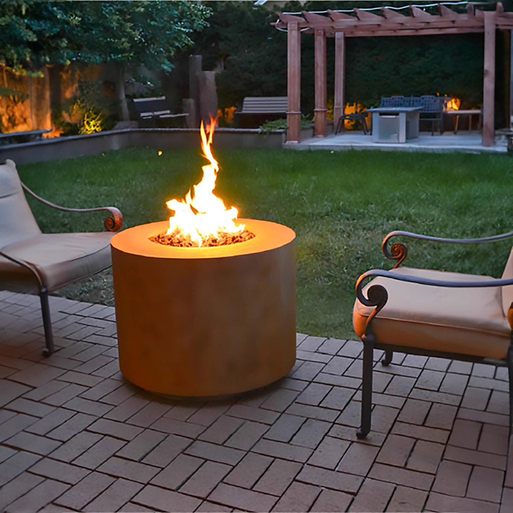 Evening patio setting with The Outdoor Plus 36" Beverly Steel Gas Fire Pit glowing warmly on a stone paver surface. Surrounded by classic outdoor chairs, this Corten steel fire pit creates an intimate and relaxing atmosphere in a lush backyard. The fire pit's round design and powerful flame make it an ideal centerpiece for outdoor entertaining.