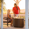 Two people enjoying a relaxed conversation around The Outdoor Plus 36" Beverly Steel Gas Fire Pit in a brown powder-coated finish. Set inside a charming white gazebo, this fire pit offers warmth and comfort as it burns brightly, creating a welcoming atmosphere for evening chats. The cozy fire pit setup is ideal for social gatherings in outdoor spaces. 