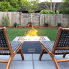 The Outdoor Plus 36" Quad Concrete Gas Fire Pit displayed in a cozy outdoor patio setting. The square fire pit is placed on a sleek modern patio with stylish wooden chairs, creating an inviting space for relaxation. The fire pit is lit with a strong natural gas flame, surrounded by decorative stones, providing warmth and elegance to the outdoor area. This image highlights the fire pit’s functionality as an outdoor heater and its ability to complement luxury outdoor furniture, perfect for enhancing backyard.