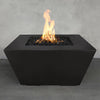 The Outdoor Plus 36" Redan Concrete Gas Fire Pit in a modern backyard setting, featuring a sleek and minimalist design with sharp angles and a matte black finish. The fire pit showcases a rectangular burner area filled with dark lava rocks, casting a warm, inviting flame that enhances the ambiance of any outdoor living space. Constructed from high-quality concrete, this fire pit is designed for durability and weather resistance, making it a perfect choice for contemporary patios and gardens.