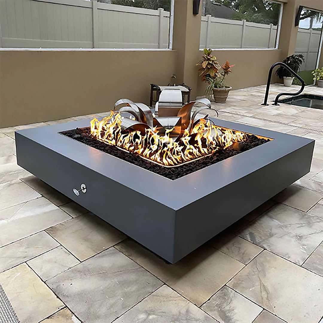 This lifestyle image showcases The Outdoor Plus 48" Cabo Square Concrete Gas Fire Pit in gray, placed in a modern backyard setting with a sleek and contemporary design. The gas fire pit features clean lines and a square shape, blending seamlessly into the outdoor patio area. Flames dance over the lava rocks, creating a warm and inviting atmosphere. Perfect for outdoor gatherings, this fire pit combines functionality and elegance, ideal for residential or commercial spaces.