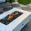 Close-up of The Outdoor Plus 48" Del Mar Concrete Gas Fire Pit in white, with focus on the flickering flames and smooth black lava rocks. The minimalist design of the fire pit blends seamlessly into modern outdoor environments. Ideal for those seeking a sleek and functional gas fire pit, this model offers an elegant flame presentation, making it perfect for upscale backyard gatherings, outdoor fire features, and patio fire pit setups.