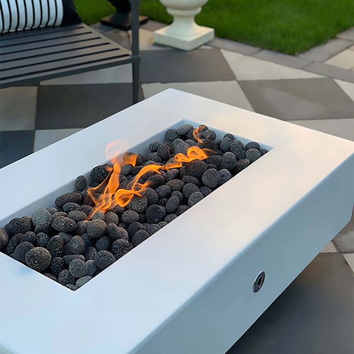 Close-up of The Outdoor Plus 48" Del Mar Concrete Gas Fire Pit in white, with focus on the flickering flames and smooth black lava rocks. The minimalist design of the fire pit blends seamlessly into modern outdoor environments. Ideal for those seeking a sleek and functional gas fire pit, this model offers an elegant flame presentation, making it perfect for upscale backyard gatherings, outdoor fire features, and patio fire pit setups.