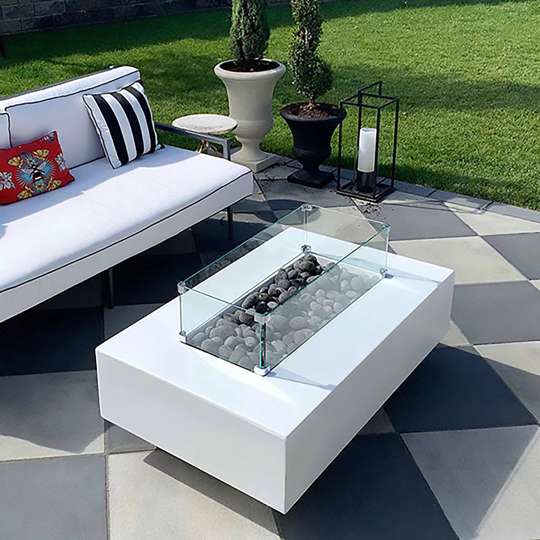 The Outdoor Plus 48" Del Mar Concrete Gas Fire Pit in white, featuring a glass wind guard around the fire basin for added safety and wind protection. Placed in a stylish outdoor seating area, the glass guard enhances the fire pit's contemporary aesthetic while allowing a clear view of the flames. This setup is ideal for high-end outdoor living areas, luxury fire pits, and patio fire pit tables.