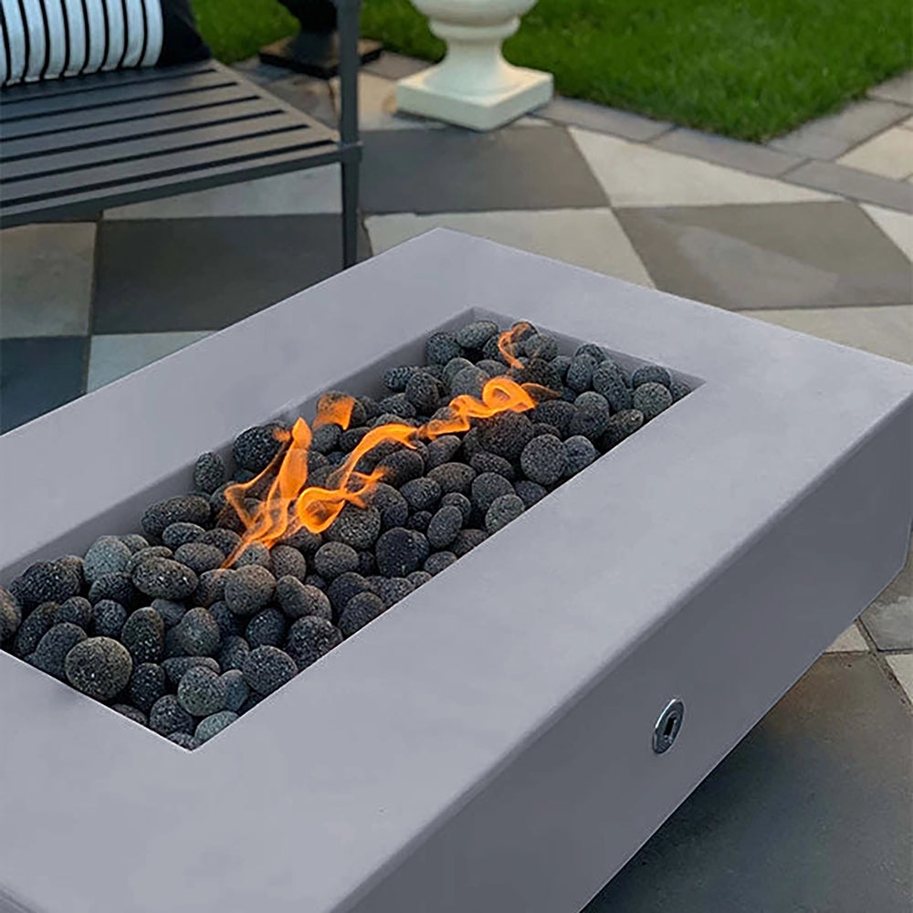 The Outdoor Plus 60-inch Del Mar Concrete Gas Fire Pit in natural gray, featuring a smooth, minimalist finish for a sophisticated outdoor fire experience. Equipped with a gas burner, this fire pit enhances backyard gatherings with a warm, inviting flame and dark pebble stones. Ideal for modern outdoor fire pit aesthetics.