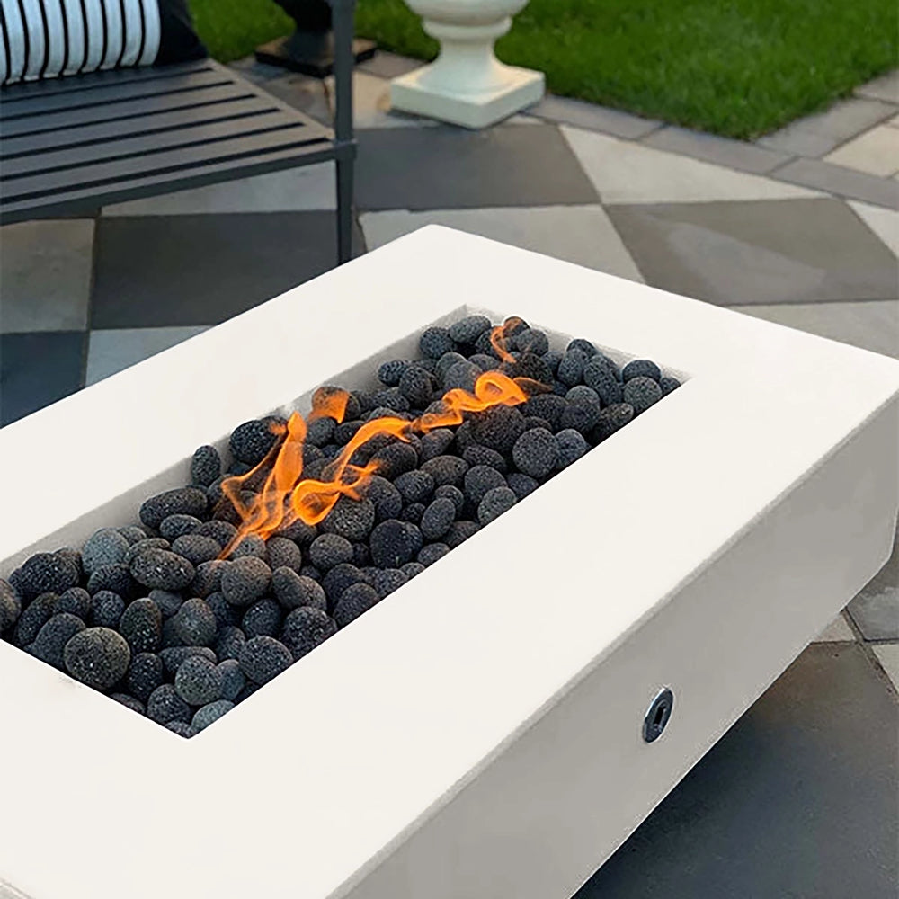 The Outdoor Plus 60-inch Del Mar Concrete Gas Fire Pit in pearl color, showcasing a clean, bright aesthetic that complements various outdoor settings. This gas fire pit provides an elegant fire display among dark lava rocks, adding warmth and luxury to patios or garden spaces. Perfect for outdoor fire features with a sleek design.