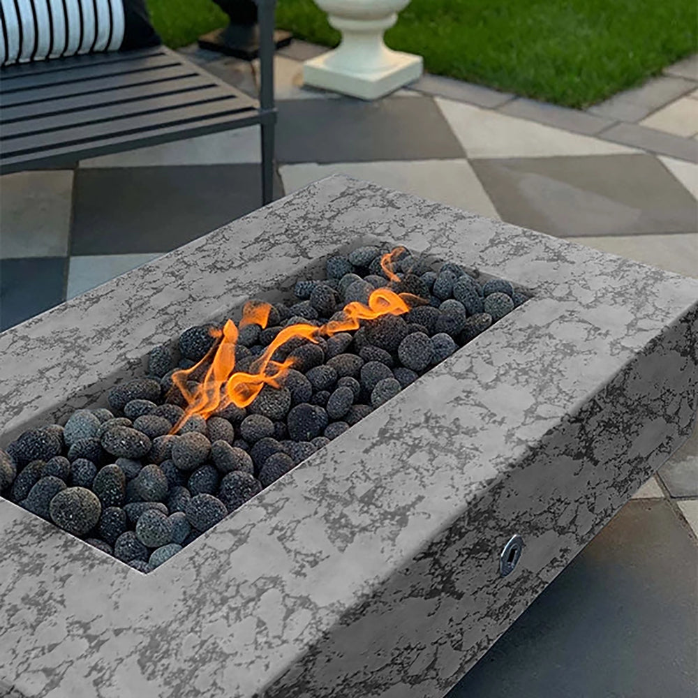 The Outdoor Plus 60-inch Del Mar Concrete Gas Fire Pit in rustic gray, featuring a natural, textured pattern that brings character to outdoor spaces. This modern fire pit uses a gas burner and dark stones to create a stunning flame effect, perfect for enhancing patio gatherings and backyard aesthetics with a unique, rustic charm.