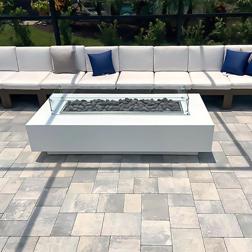 The Outdoor Plus 60-inch Del Mar Concrete Gas Fire Pit in a luxurious outdoor seating area. Featuring a sleek rectangular design with a glass wind guard and burning lava rocks, this gas fire pit provides a warm and modern focal point for the patio, surrounded by comfortable seating, perfect for gathering.